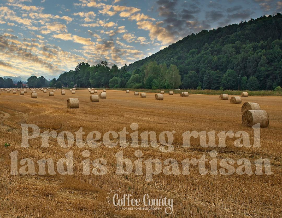 Large field with rolled-up straw bales and a wooded ridge in the back